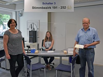 Das Wahlamt im Sitzungssaal ist „coronagerecht“ eingerichtet: Andrea Müller (l.) und Manfred Leutnant (r.) aus dem Fachdienst Organisation vor einem Arbeitsplatz, an dem die Auszubildende Johanna Schönberger hinter einer Schutzscheibe sitzt. Foto: Stadt Lippstadt
