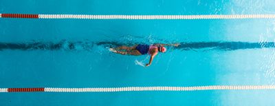 Person schwimmt Bahn im Schwimmbad, Perspektive von oben