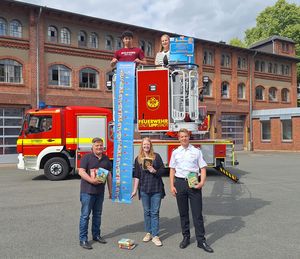 Hoch hinaus in den Sommerferien: Gemeinsam mit vielen fleißigen Leserinnen und Lesern soll der Bücherturm so hoch werden wie die Drehleiter der Lippstädter Feuerwehr.  Praktikant Anwar Oun,  Leiterin Tahnee Exner (beide oben) sowie Bürgermeister Arne Moritz, Kathrin Heberle (Stadtbücherei) und Boris Surendorf (Feuerwehr Lippstadt) drücken die Daumen für einen neuen Rekord. Foto: Stadt Lippstadt
