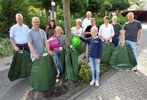 Andreas Ferch, Ute Ehring, Sabine Hense-Ferch, Thomas Bollwerk-Reichwein, Ulrike Grundmann, Doris Fockers und Claus Lößmann (v.l.) wollen sich gemeinsam mit weiteren Nachbarn verstärkt um die Bäume in ihren Straßen kümmern. Von Christian Kleineheilmann (l.) und Fabian Nienaber (r.) vom städtischen Fachdienst Grünflächen, Spielen und Sport erhielten sie dafür jetzt die passenden Bewässerungssäcke. Hannah und Bruno Lößmann befüllten den ersten Sack direkt mit Wasser. Foto: Stadt Lippstadt