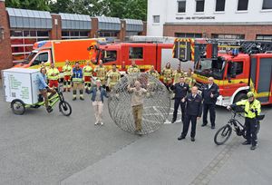 Mit guten Wünsche und viel Erfolg für seinen „Promise Walk“ wurde Aktionskünstler Arnd Drossel (in der Drahtkugel) von Vertretern von Feuerwehr und Rettungsdienst sowie von Brigit Specovius, Koordinatorin des Klimabündnisses bei der Stadt Lippstadt (l. neben der Drahtkugel), aus Lippstadt verabschiedet. In der Feuer- und Rettungswache an der Geiststraße hatten der Künstler und seine Mitstreiter die Drahtkugel bis zum Start der nächsten Etappe lagern und reparieren können.  Foto: Stadt Lippstadt