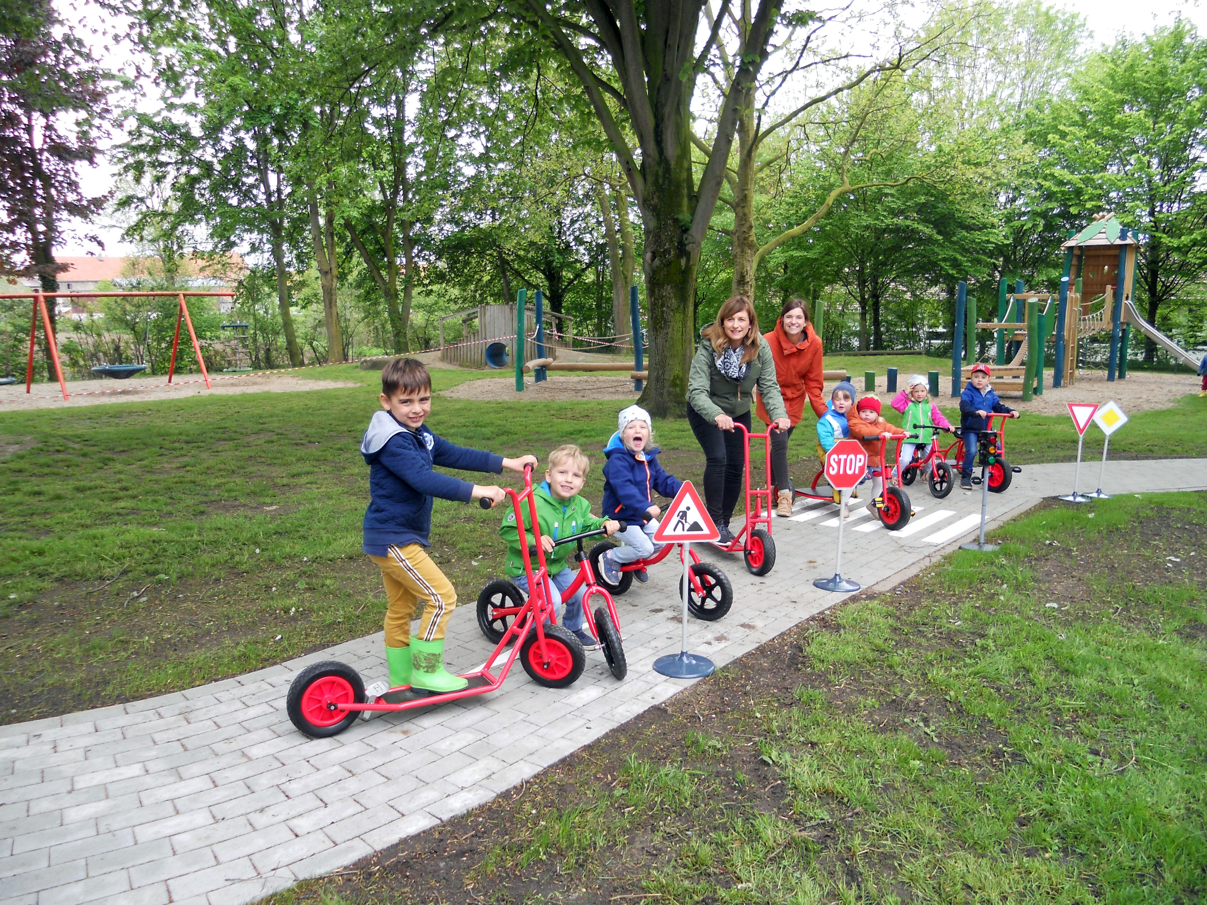„Rennstrecke Hurra!“ – auf Rollern und Laufrädern sind die Kinder der Kita Rixbeck bereits startklar, um die neue Rennstrecke zu erkunden. Einrichtungsleiterin Mirjana Bruno (l.) und Fördervereinsvorsitzende Anna Jungemann (r.) freuen sich ebenfalls über die Fertigstellung. Foto: Kita Rixbeck