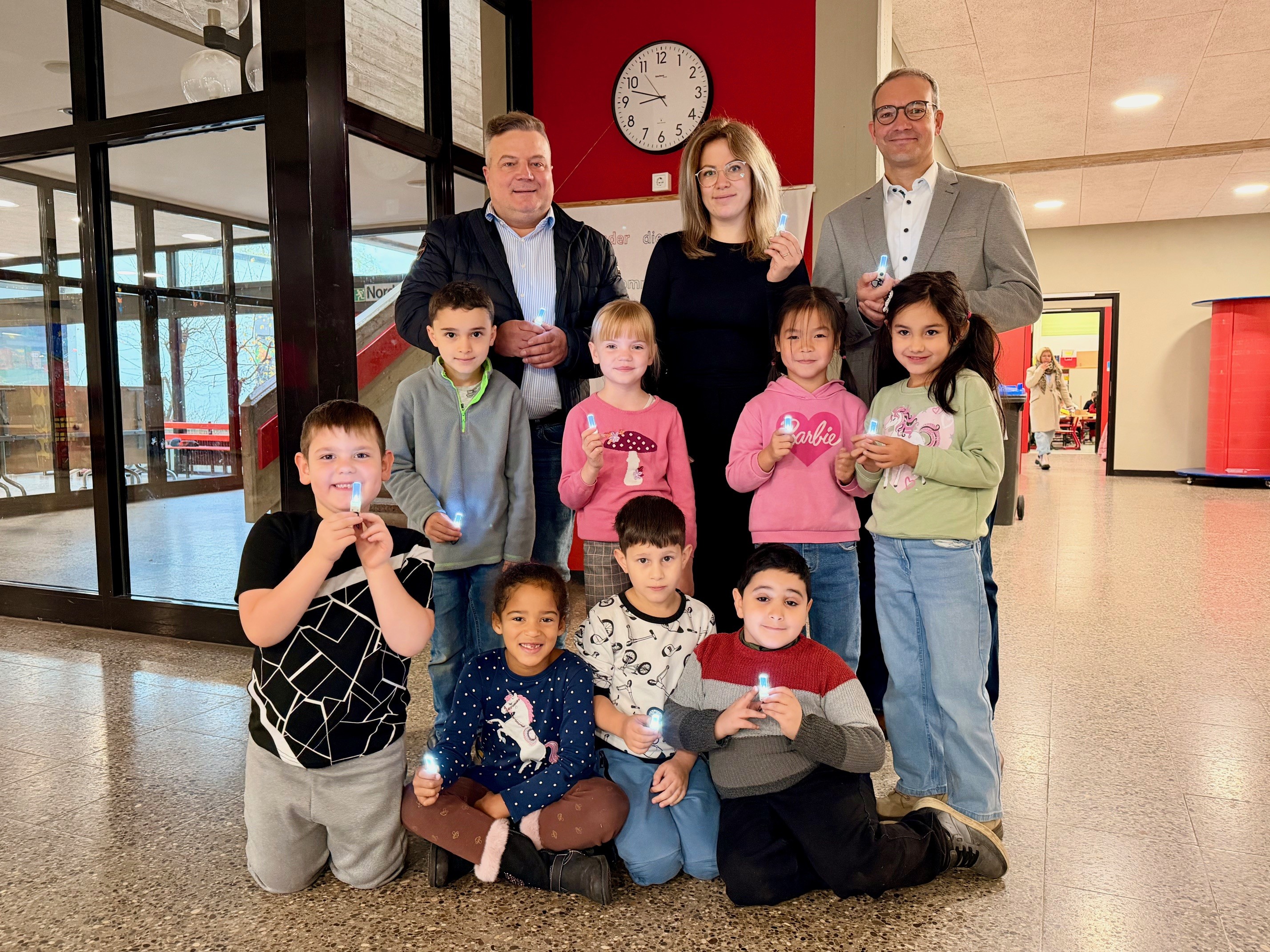 Sie sind so hell, dass ihr Leuchten sogar bei Tageslicht gut erkennbar ist: Schülerinnen und Schüler aus der ersten Klasse von Konrektorin Carina Krause probierten gemeinsam mit Bürgermeister Arne Moritz und Thomas Raulf von der Sparkasse Hellweg-Lippe die LED-Blinkis aus. Foto: Stadt Lippstadt